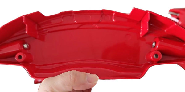 Red  aluminium brake covers for Tesla held by a hand with a blurred background