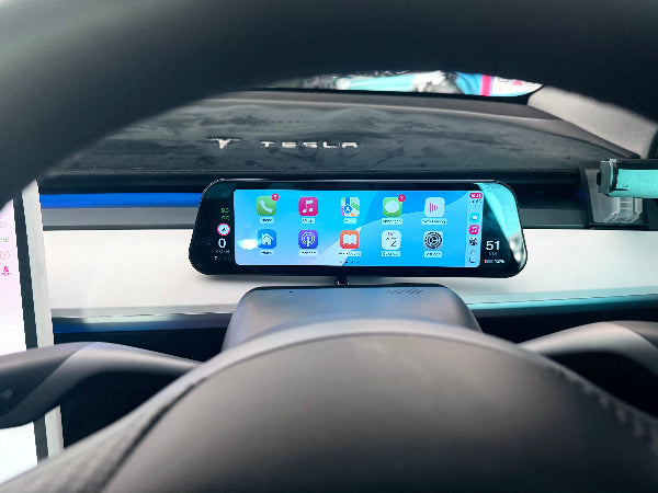 Car dashboard with a touchscreen display showing app icons, with Tesla logo visible.