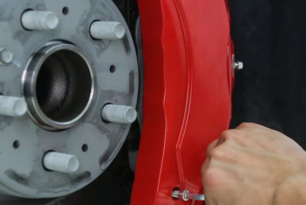 Close-up of a red brake caliper being attached to a car wheel hub.