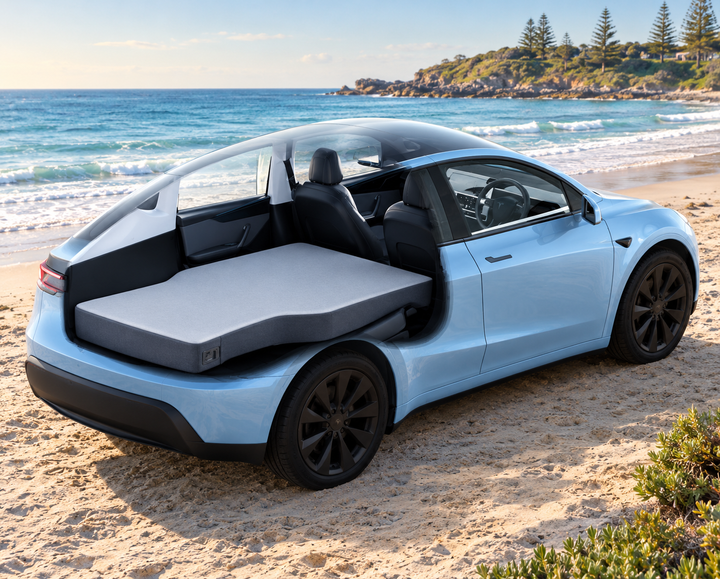 Flat camping mattress fitted from boot to front seats in a right-hand-drive Tesla Model Y on an Australian beach